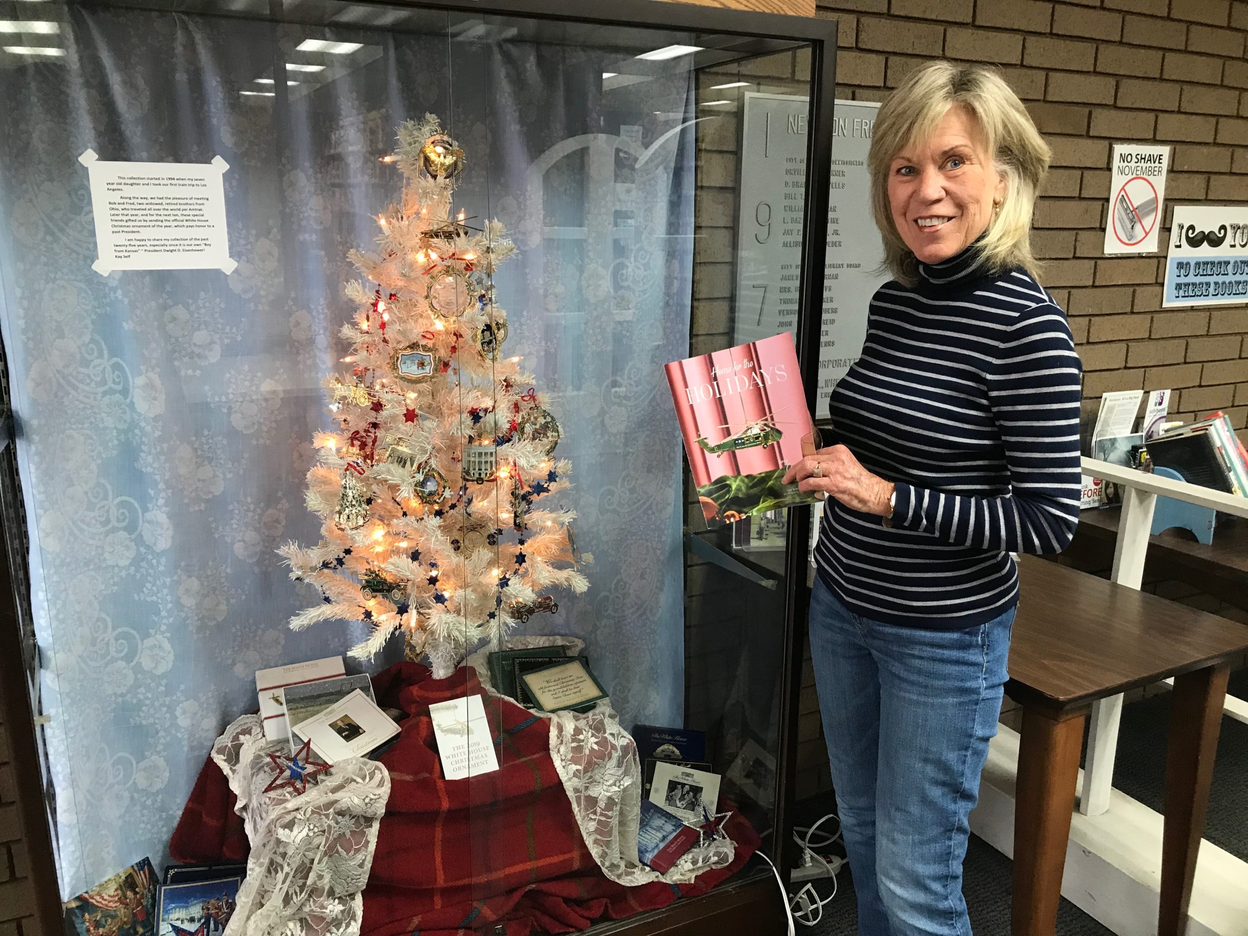 Kay Self poses for a photo with her Christmas ornament display. White House commemorative Christmas ornaments on a white artificial tree.