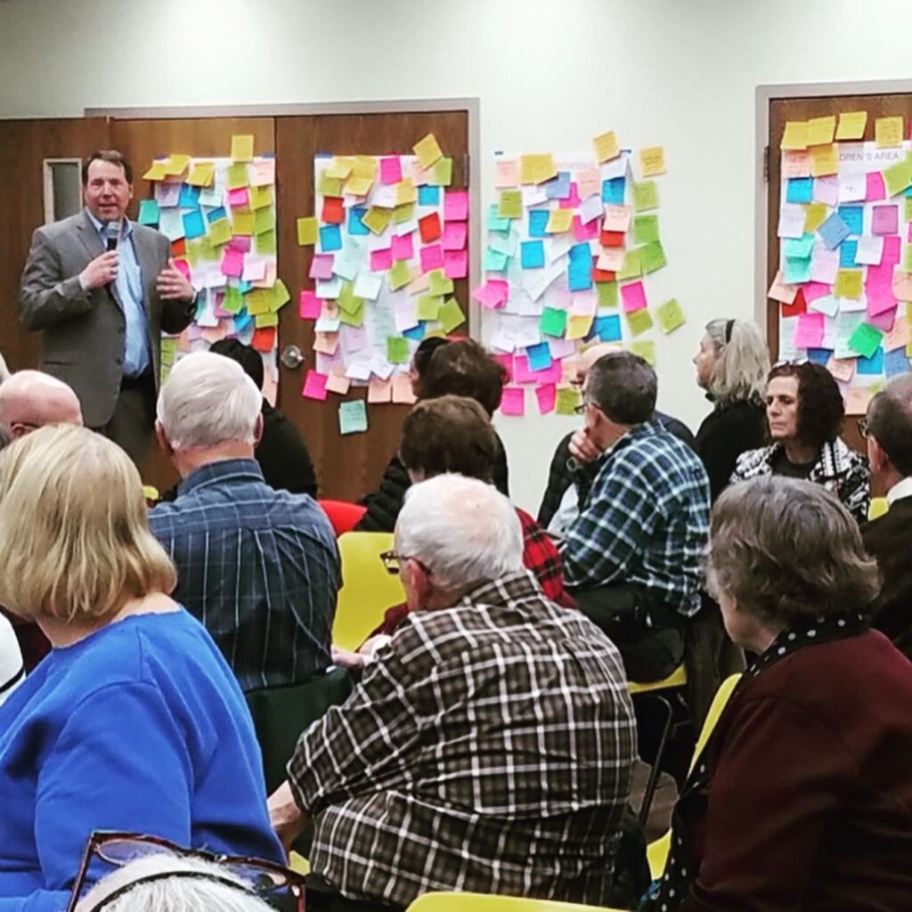 Peter Bolek speaks to attendees a community meeting held in February. Lots of sticky notes are stuck to the wall behind him.