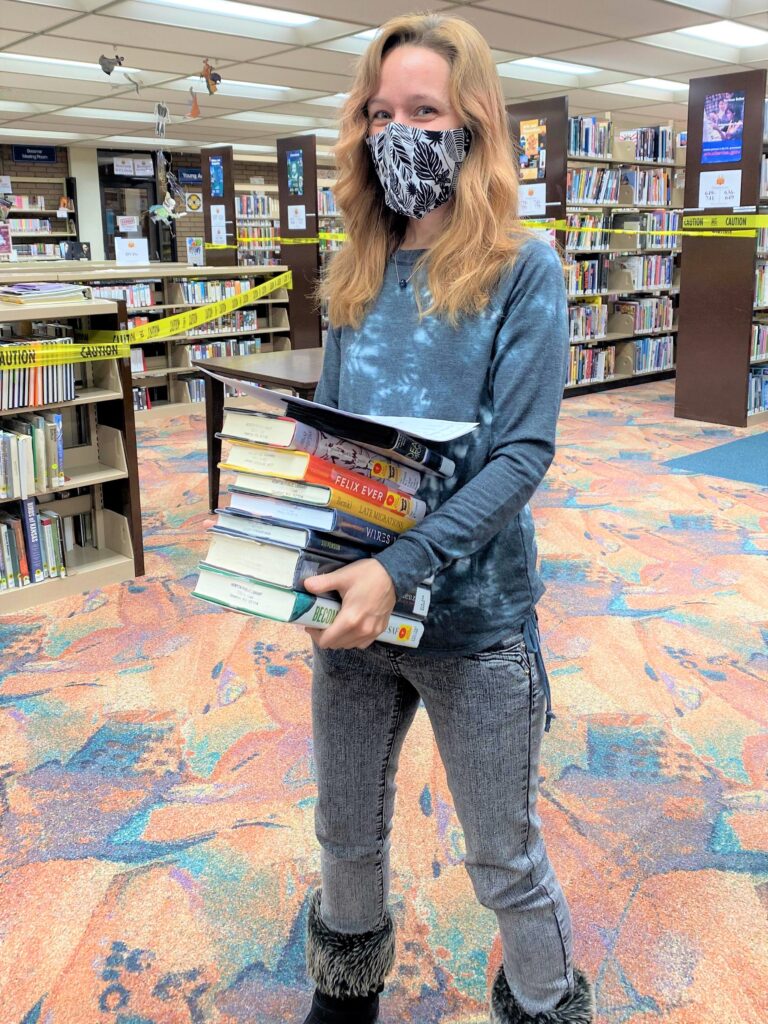 A smile Newton Public Library aide carries a stack of books.