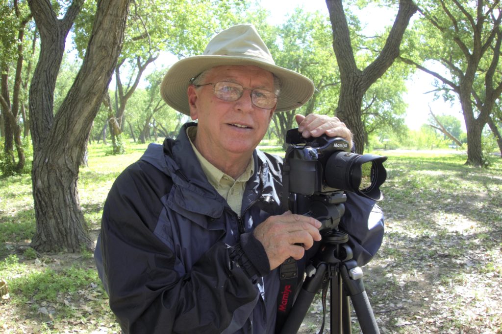 Photographer Dale Strattman is pictured wearing a floppy hat and holding a large camera on a tripod.