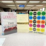 Covers of "The Surgeon," "Braiding Sweetgrass," and "Super Sad True Love Story are pictured sitting on a table.