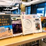 Each of the February 2025 book club selections is displayed side by side. From left to right, the books are: A Deadly Bone to Pick, Homeland, The Last Stargazers, Devil on the Cross, and Before I Let Go.